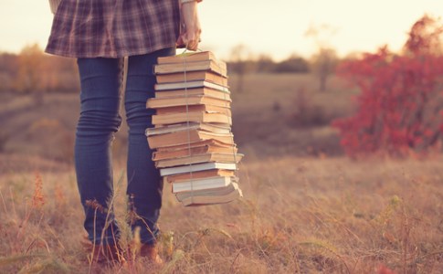 person in a field carrying stack of books wrapped in string